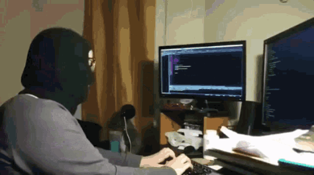 Hacker in a balaclava typing away at a desktop battlestation